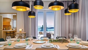 Un coin repas avec une table dressée pour six personnes, de grandes lampes suspendues noires et une vue sur l’extérieur grâce à une grande fenêtre.