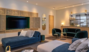 Une chambre d’hôtel moderne dotée d’un grand téléviseur à écran plat, d’un mur revêtu de panneaux en bois, d’un miroir, d’un coin bar avec des verres et de sièges confortables.