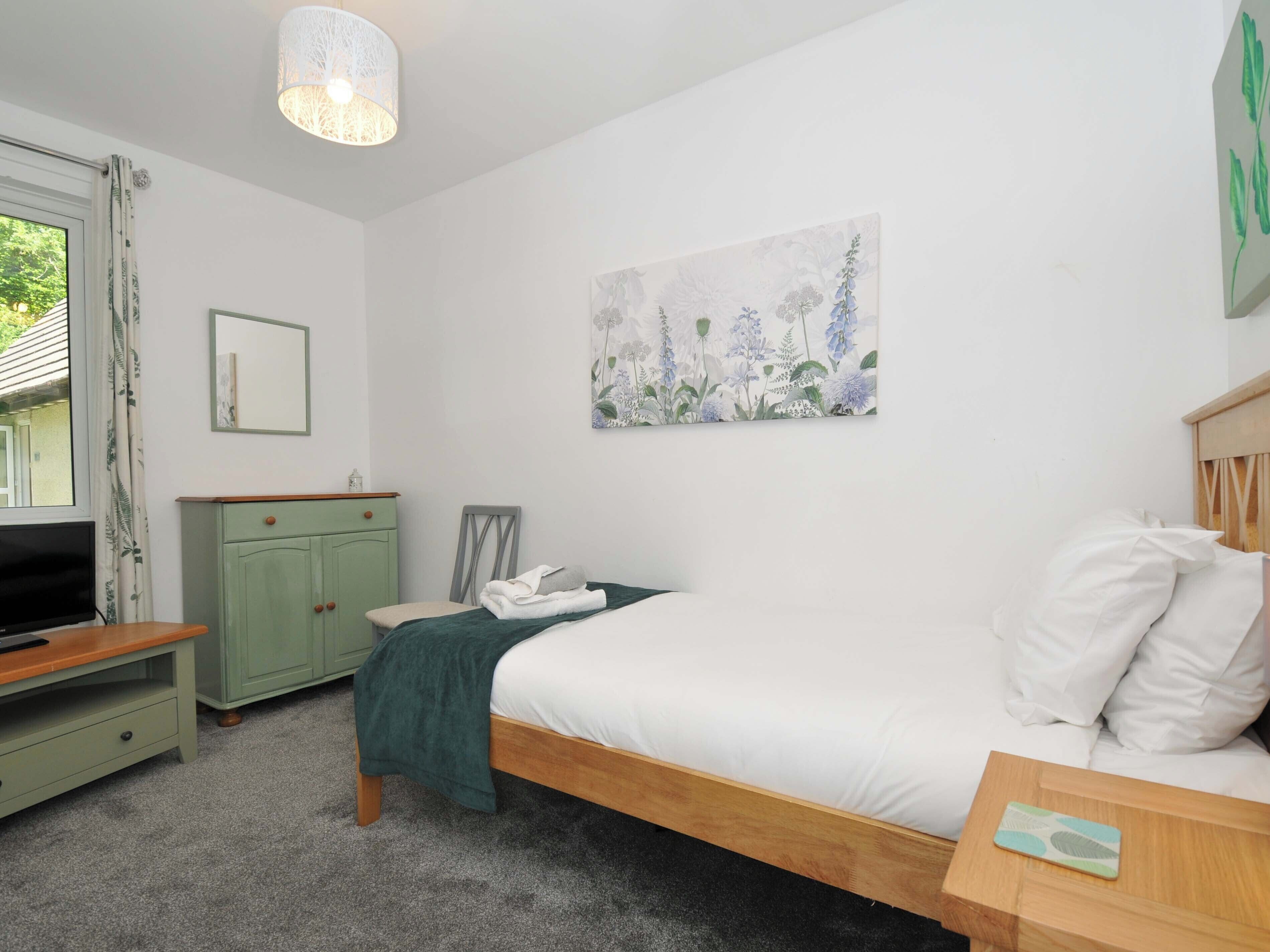 A bedroom with a bed, a desk, a TV, a cabinet, and a painting on the wall.