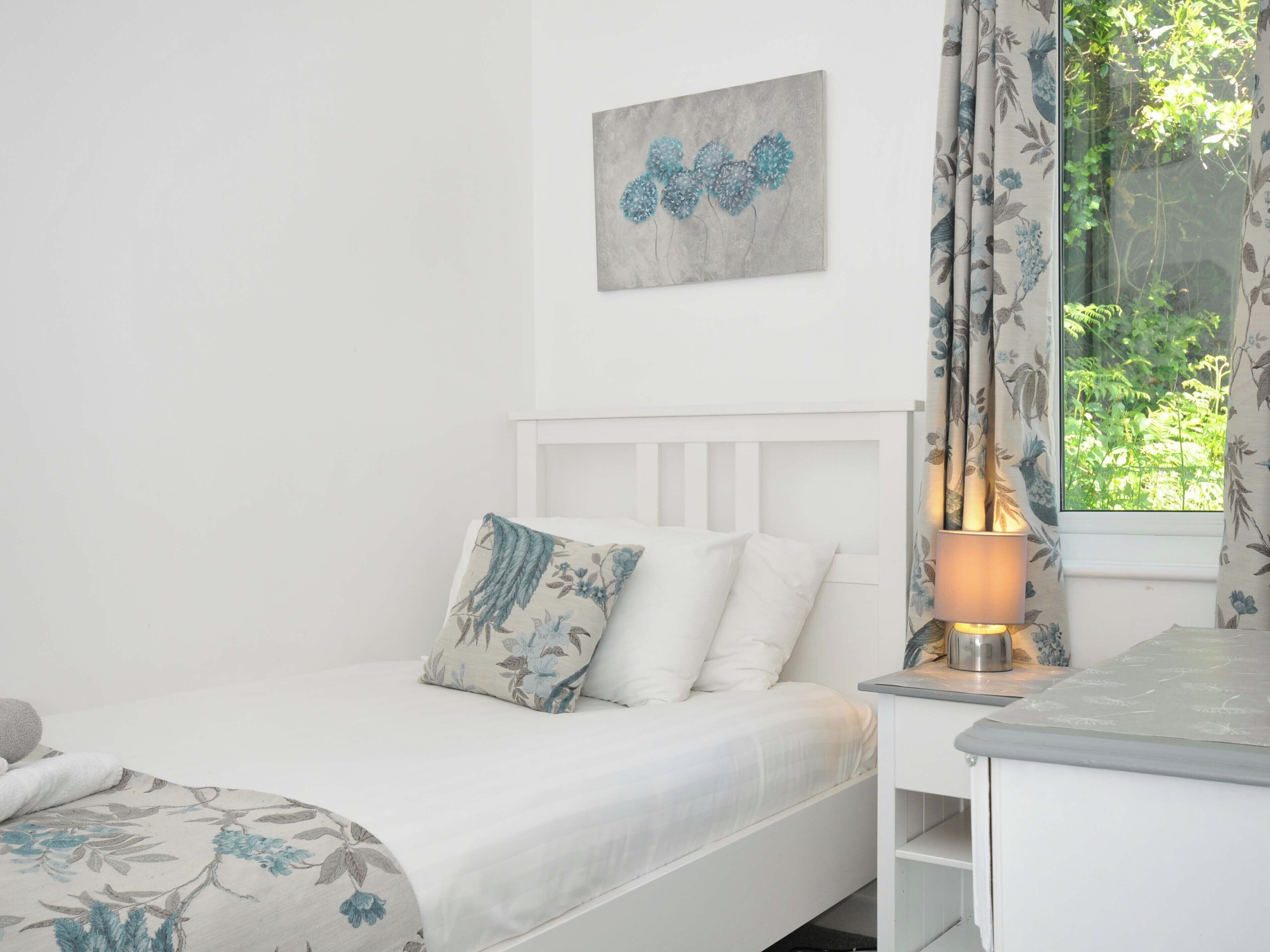 A bedroom with a bed, a bedside table, a lamp, and a window with curtains.