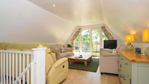 A cozy loft bedroom with a sofa, a small table, a TV, and a cabinet. - 60 Valley Lodge (Gunnislake)