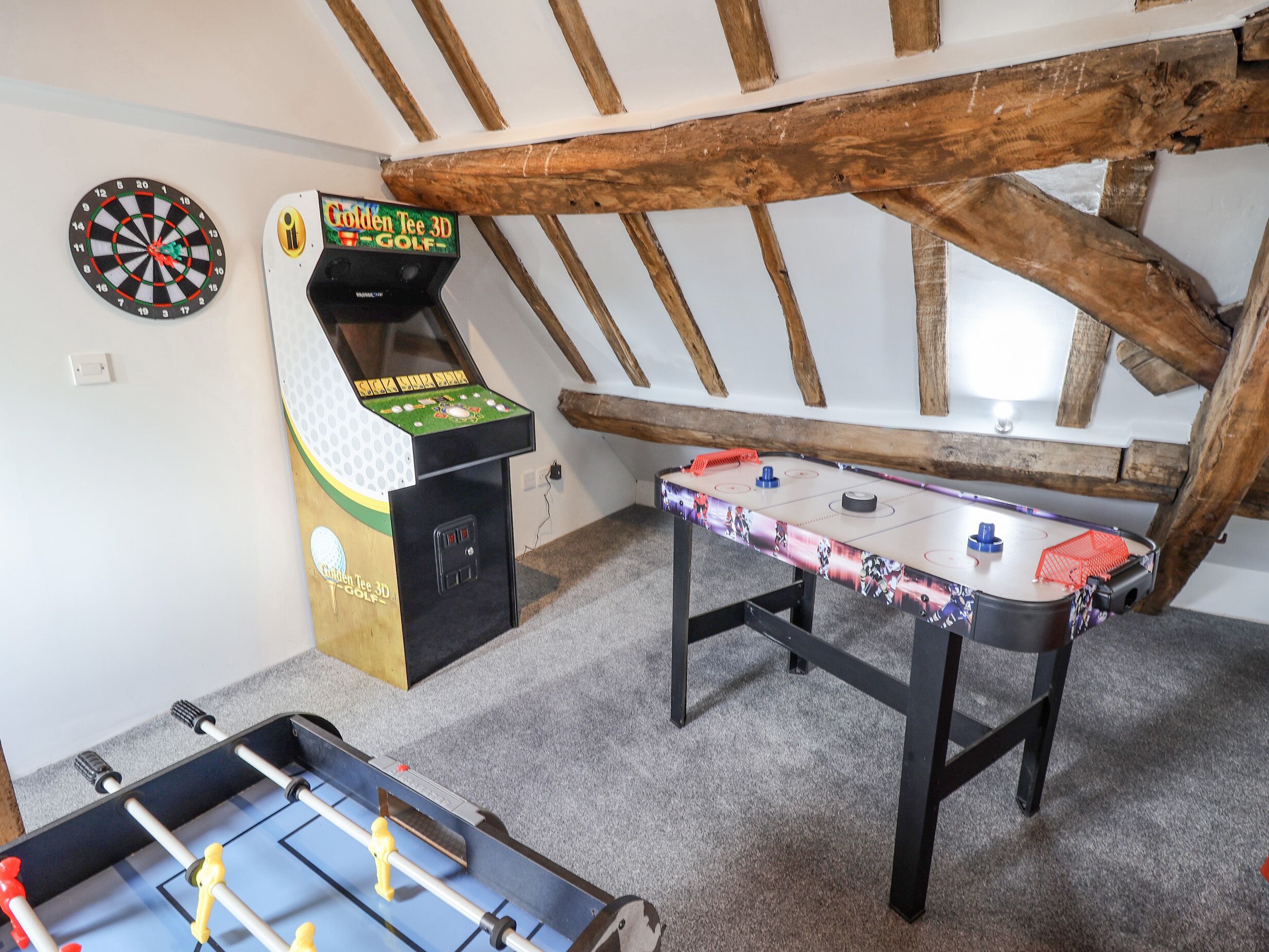 A room with a foosball table, a dartboard, and a 3D golf arcade game.