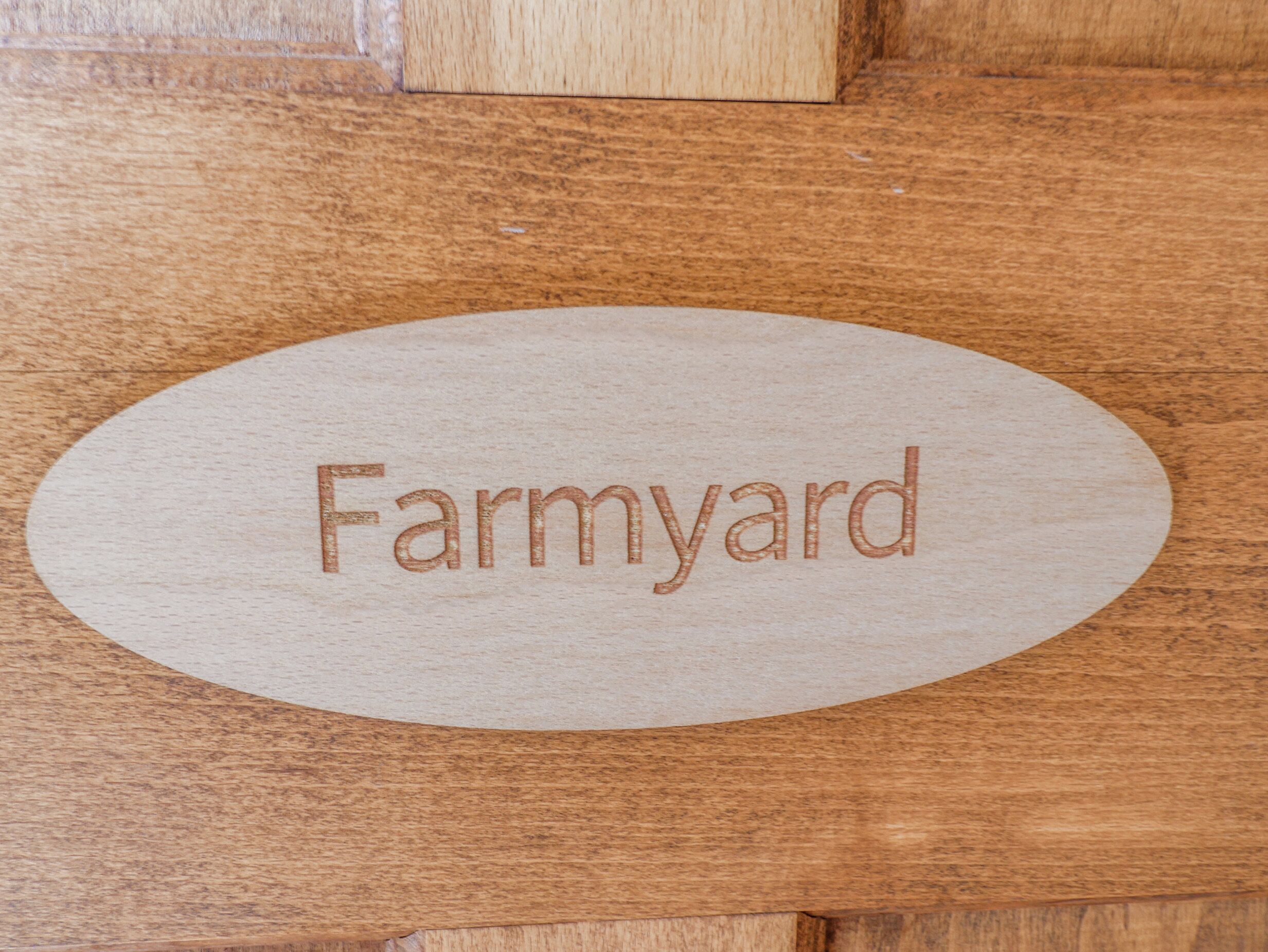 An oval wooden plaque with the word "Farmyard" engraved on it.