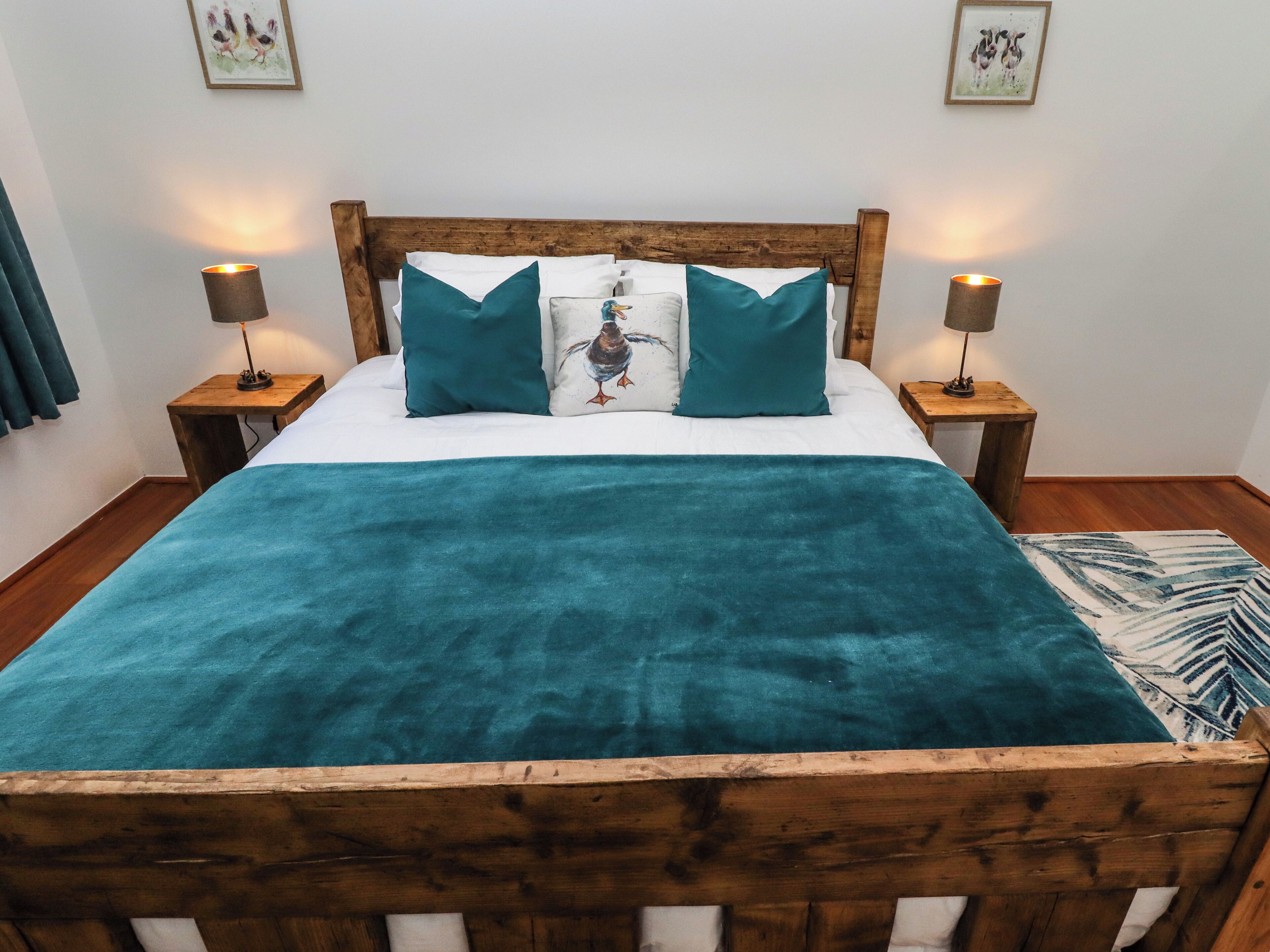 A bed with a wooden headboard, teal bedding, and two bedside lamps.