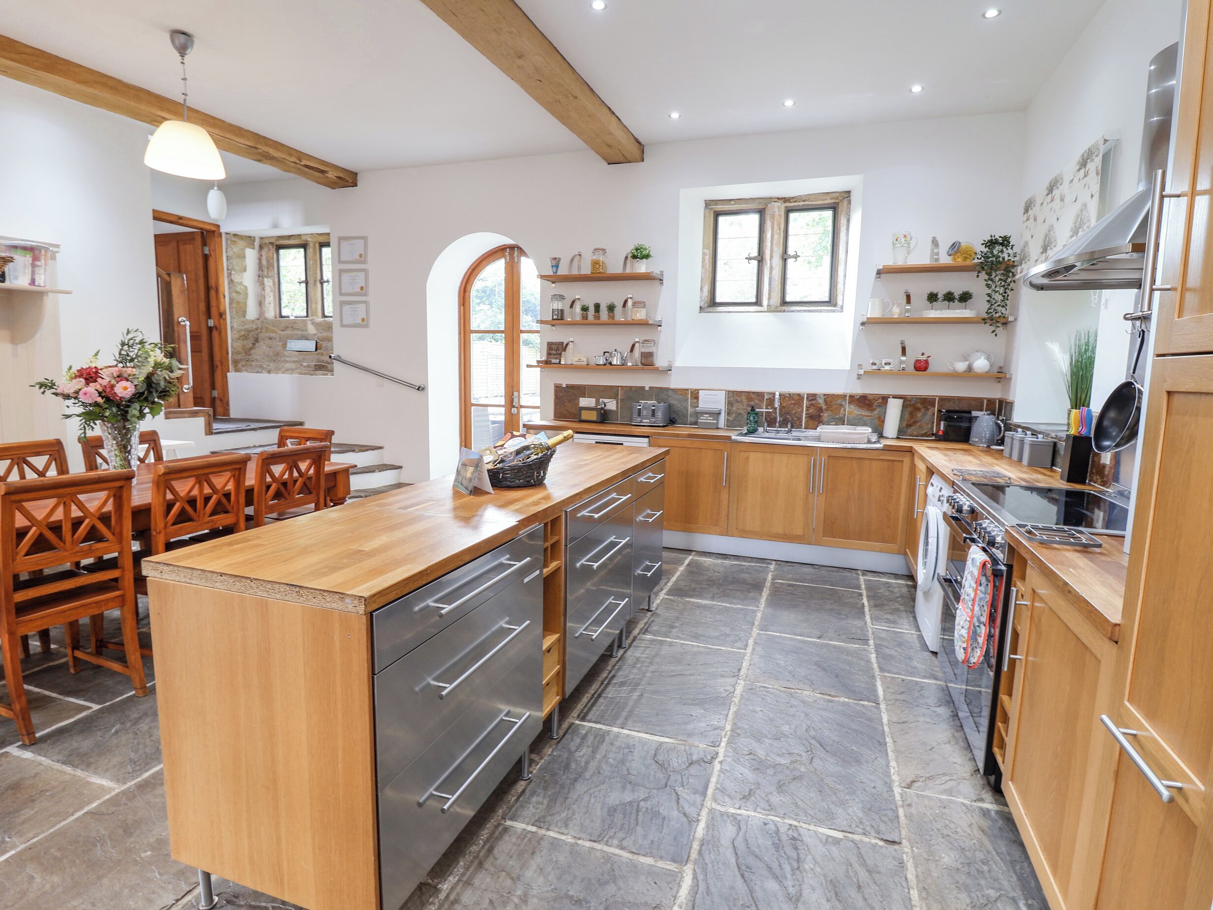 A modern kitchen with wooden cabinetry, a central island with a sink, and a dining area with wooden chairs.
