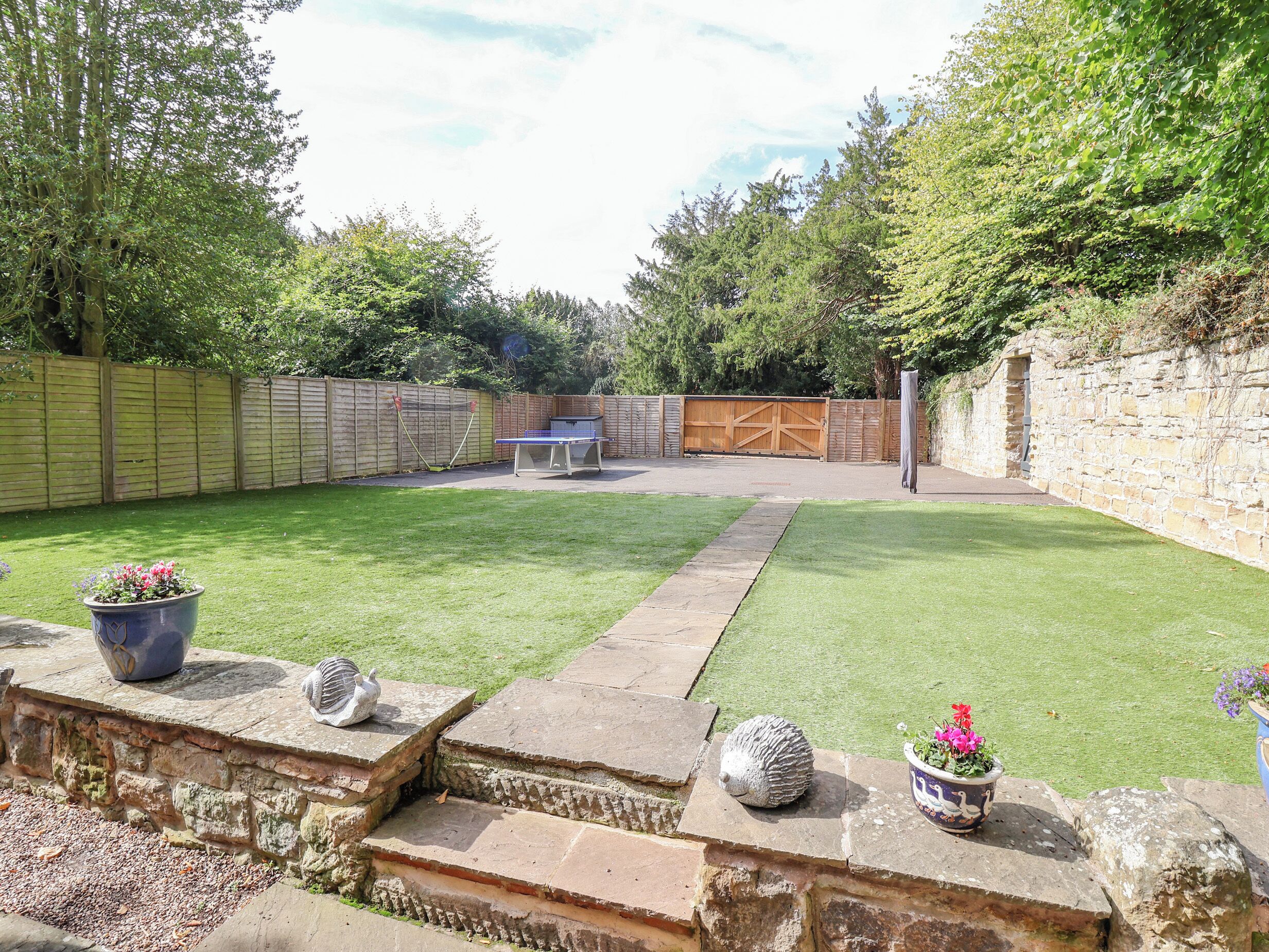A backyard with a ping pong table, a stone wall, and a wooden fence.