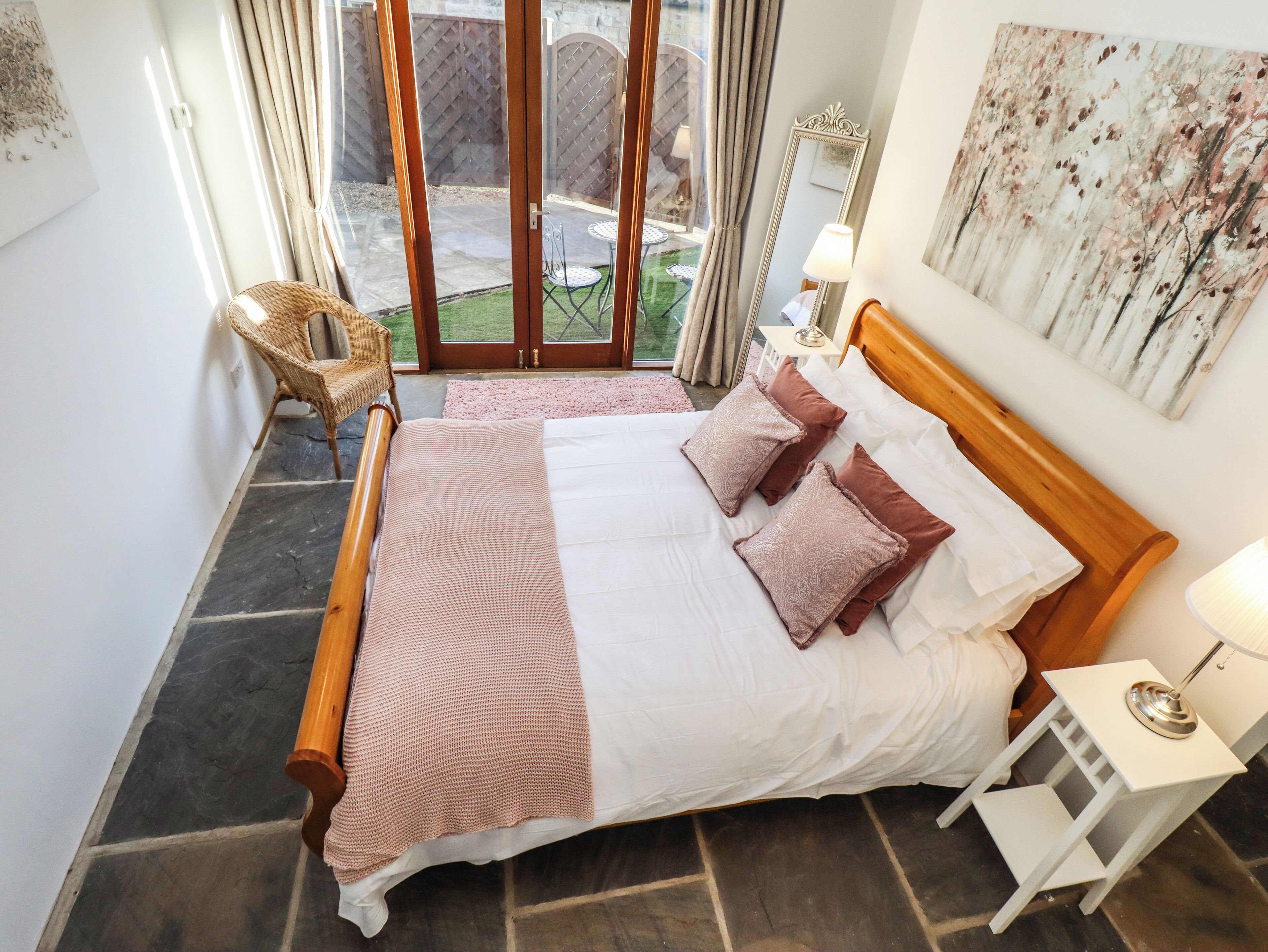 A bedroom with a wooden bed, white bedding, and a view of the outdoors through a glass door.