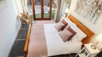 A bedroom with a wooden bed, white bedding, and a view of the outdoors through a glass door.