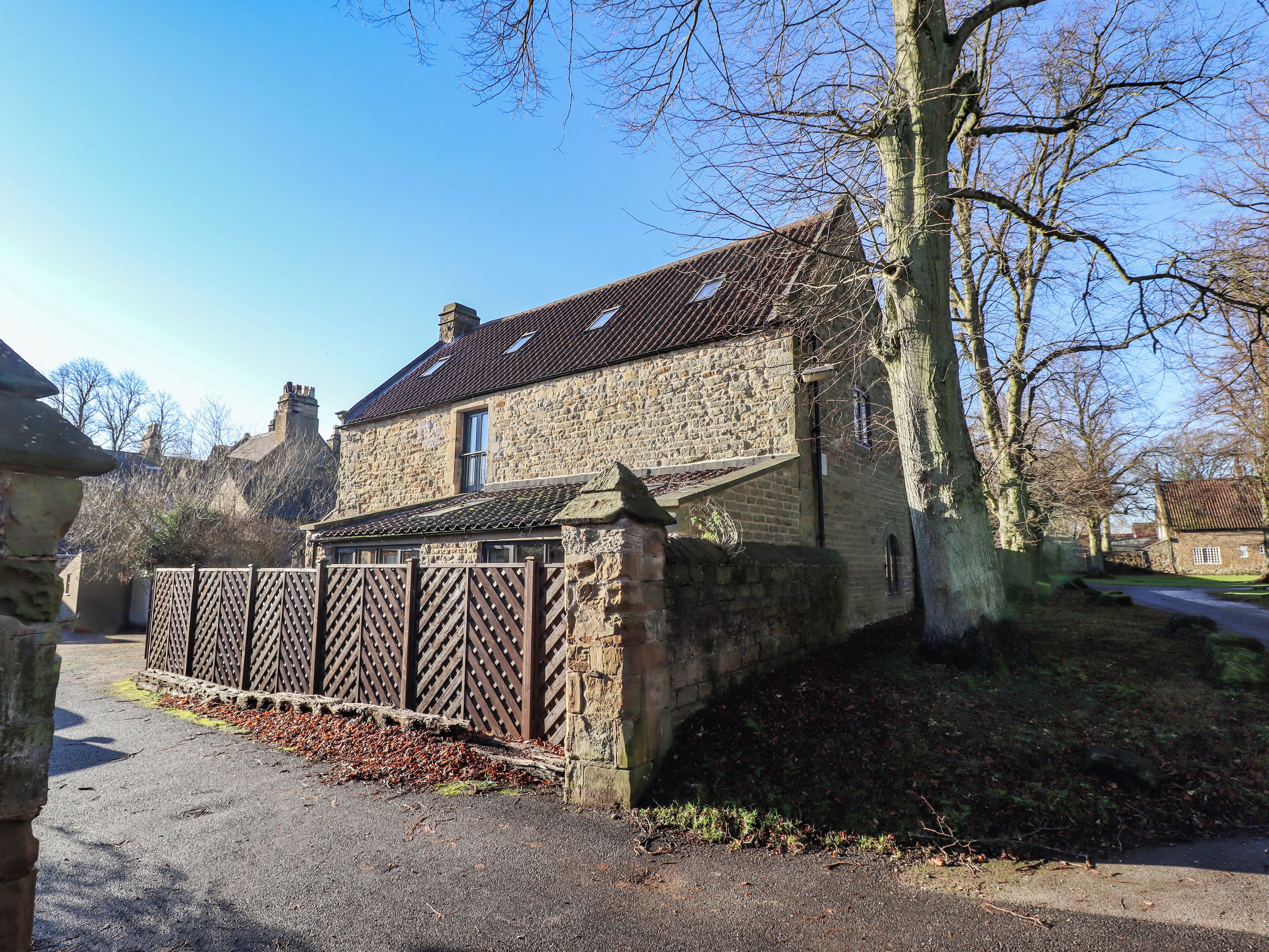 A stone building with a tiled roof, a gated entrance, and a tree in the foreground.