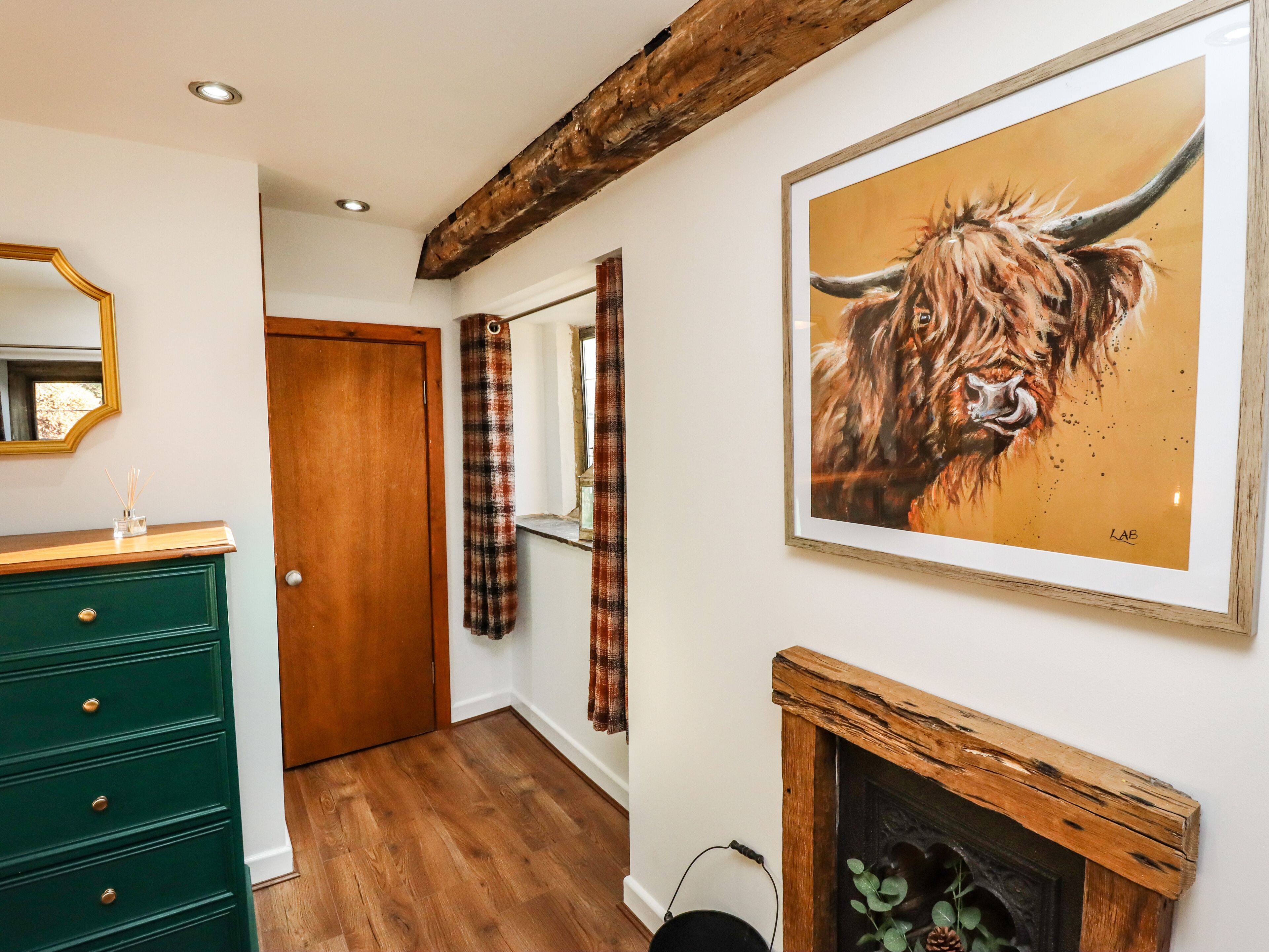 A hallway with a wooden floor, a green dresser, a mirror, plaid curtains, and a framed painting of a bull.