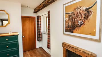 A hallway with a wooden floor, a green dresser, a mirror, plaid curtains, and a framed painting of a bull.