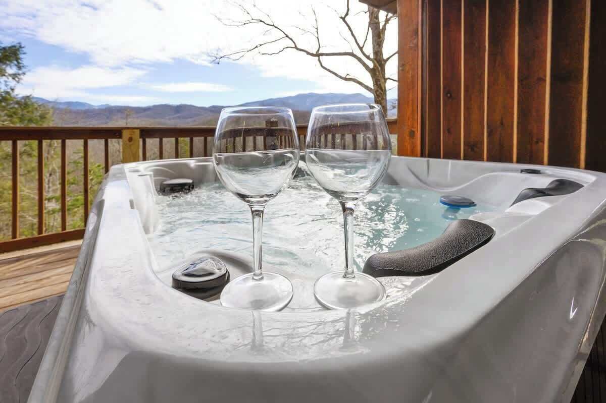 Ein Whirlpool mit zwei leeren Weingläsern auf einer Holzterrasse mit Blick auf die Berge.