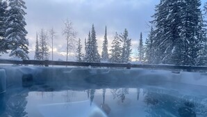 A hot tub surrounded by snow-covered trees and a wooden fence. - Lazy Moose Lodge - Luxurious, stylish mountain home with hot tub (Golden)