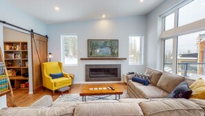 A cozy living room with a fireplace, a yellow armchair, a sofa, and a bookshelf. - Lazy Moose Lodge - Luxurious, stylish mountain home with hot tub (Golden)