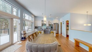 A modern kitchen with a central island, large windows, and a dining area with a bench. - Lazy Moose Lodge - Luxurious, stylish mountain home with hot tub (Golden)