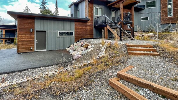 A modern two-story house with a wooden deck, a covered outdoor area, and a stone pathway leading to the entrance. - Lazy Moose Lodge - Luxurious, stylish mountain home with hot tub (Golden)