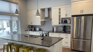 A modern kitchen with a large island, stainless steel appliances, and yellow stools. - Lazy Moose Lodge - Luxurious, stylish mountain home with hot tub (Golden)