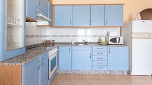 Een keuken met blauwe kastjes, een granieten aanrecht, een magnetron en een koelkast.