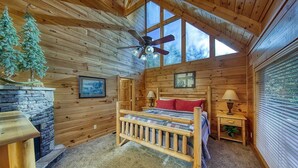Camera accogliente in legno con un letto di legno, un camino in pietra e un'ampia finestra.