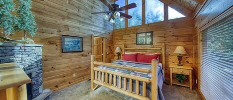 Un dormitorio de cabaña de troncos acogedor, con una cama de madera, una chimenea de piedra y un ventanal grande.