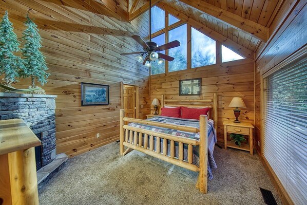 A cozy log cabin bedroom with a wooden bed, a stone fireplace, and a large window. - Views! Sleeps 16! 4bed 4bath. 5 Min to Pigeon Forge! (Sevierville)