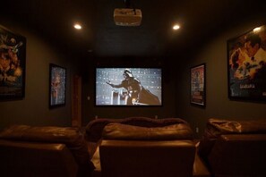A dark room with a large screen displaying a movie, leather chairs, and movie posters on the walls. - Views! Sleeps 16! 4bed 4bath. 5 Min to Pigeon Forge! (Sevierville)
