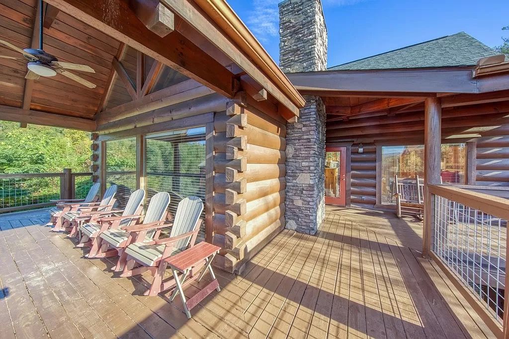 A log cabin with a deck, outdoor seating, and a stone chimney.