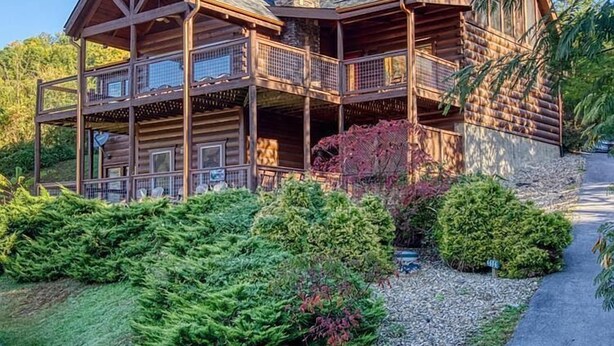 Una baita di tronchi con un portico a due piani, un camino in pietra e un giardino curato.