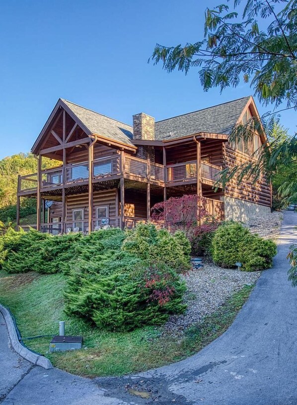 A log cabin with a two-story porch, stone chimney, and a well-maintained garden. - Views! Sleeps 16! 4bed 4bath. 5 Min to Pigeon Forge! (Sevierville)