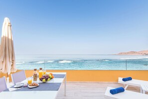A balcony with a table set for breakfast, overlooking the ocean.