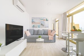 A modern living room with a flat-screen TV, grey sofa, and a round coffee table with a plant.