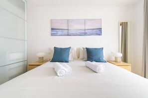 A hotel room with a large bed, two nightstands, a wall-mounted painting, and a mirror.