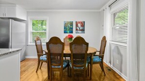 A dining area with a round table and four chairs, a refrigerator, and two windows with blinds. - Modern Charm & Garden View sleeps 6 (Greensboro)