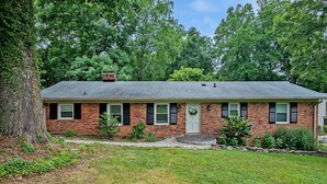 A single-story brick house with a front door, a small porch, and a chimney. - Modern Charm & Garden View sleeps 6 (Greensboro)