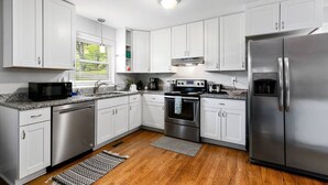 A modern kitchen with white cabinets, stainless steel appliances, and a granite countertop. - Modern Charm & Garden View sleeps 6 (Greensboro)