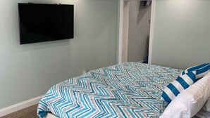 Et soveværelse med seng, loftventilator, vægmonteret TV og en dør.