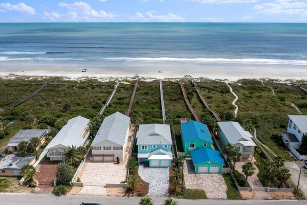 A coastal residential area with houses aligned along a beach, featuring a sandy driveway and a clear view of the ocean. - Just Beachy: Stunning 4BR Oceanfront Home + Private Pool (St. Augustine)