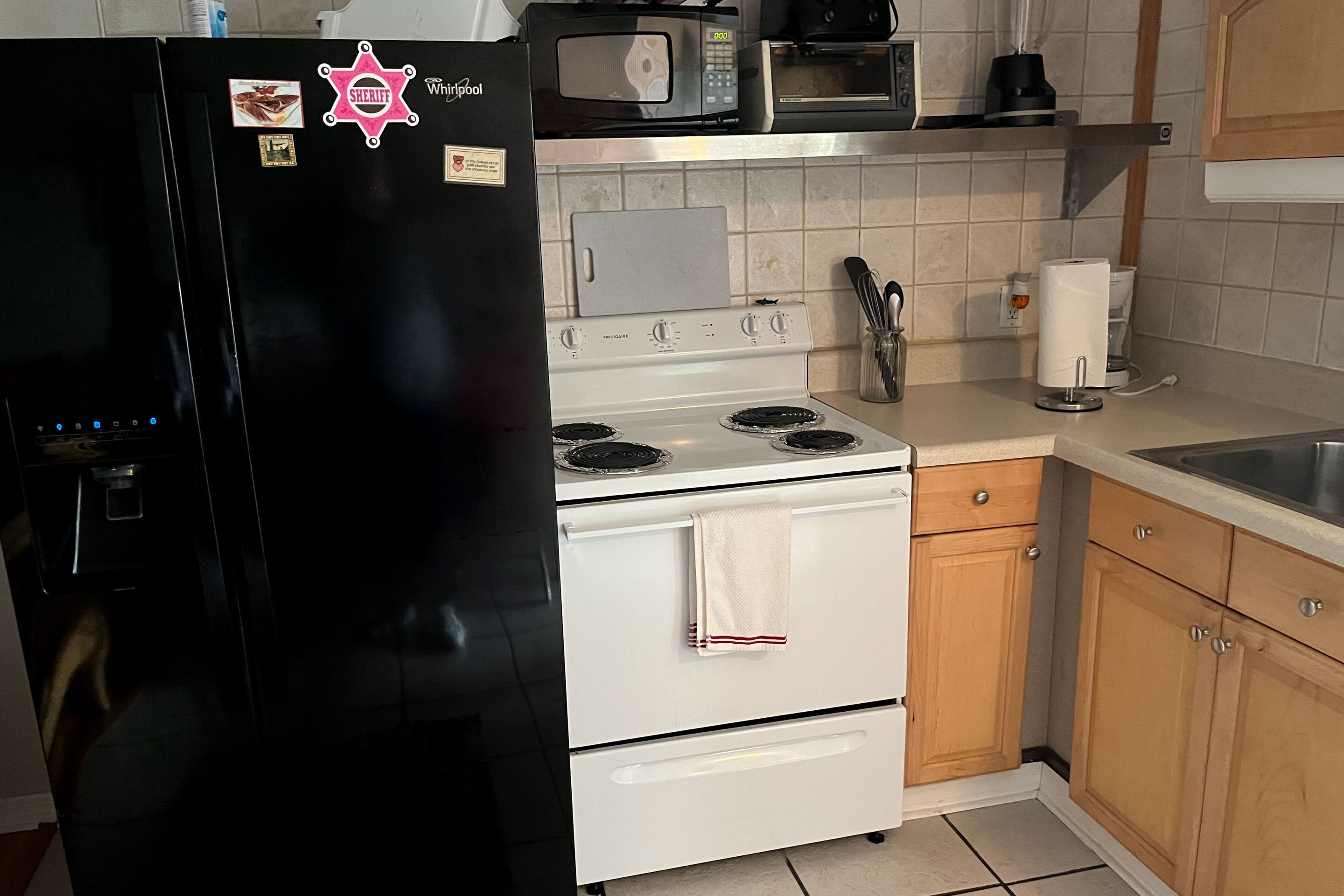 Una cocina con un refrigerador negro, estufa blanca y armarios de madera.