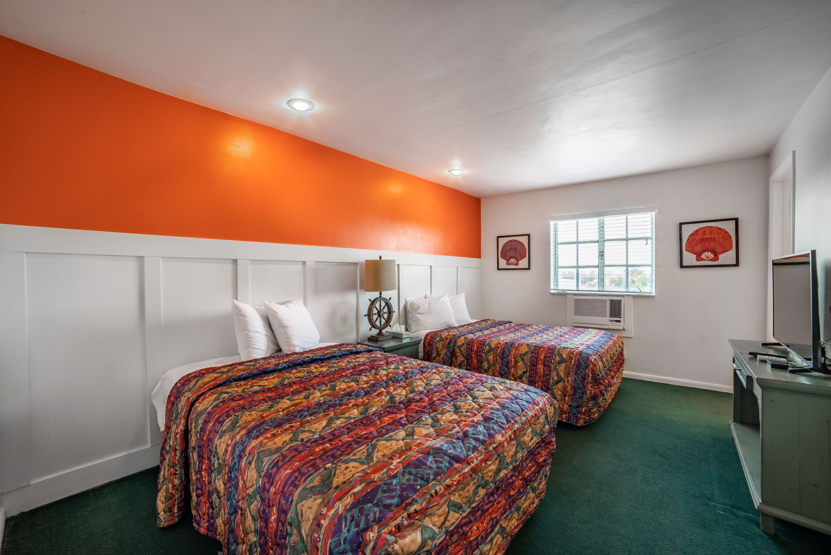 A hotel room with two beds, a large window, a desk, and a television.