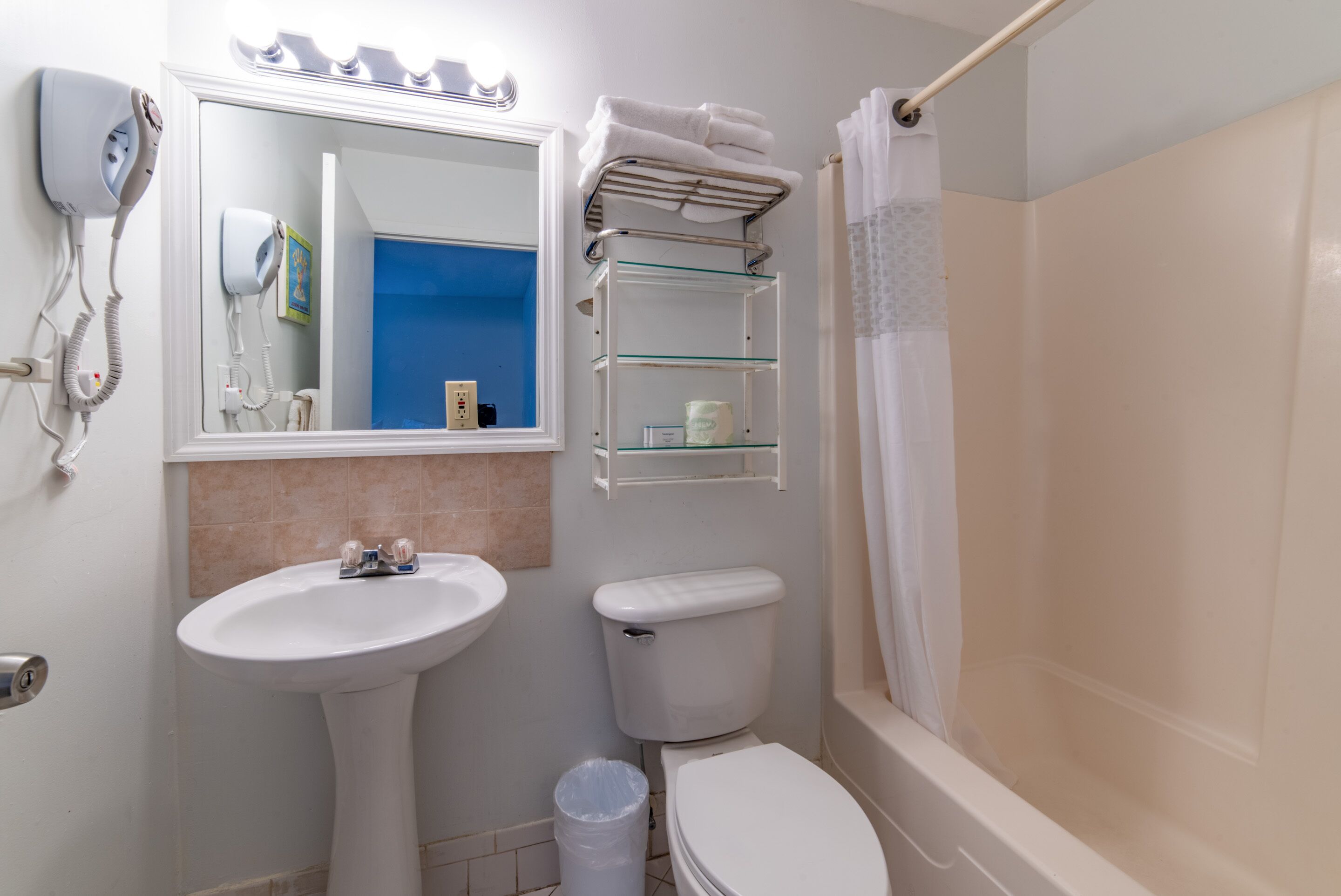 Un baño con lavamanos pedestal, inodoro y estante de vidrio.