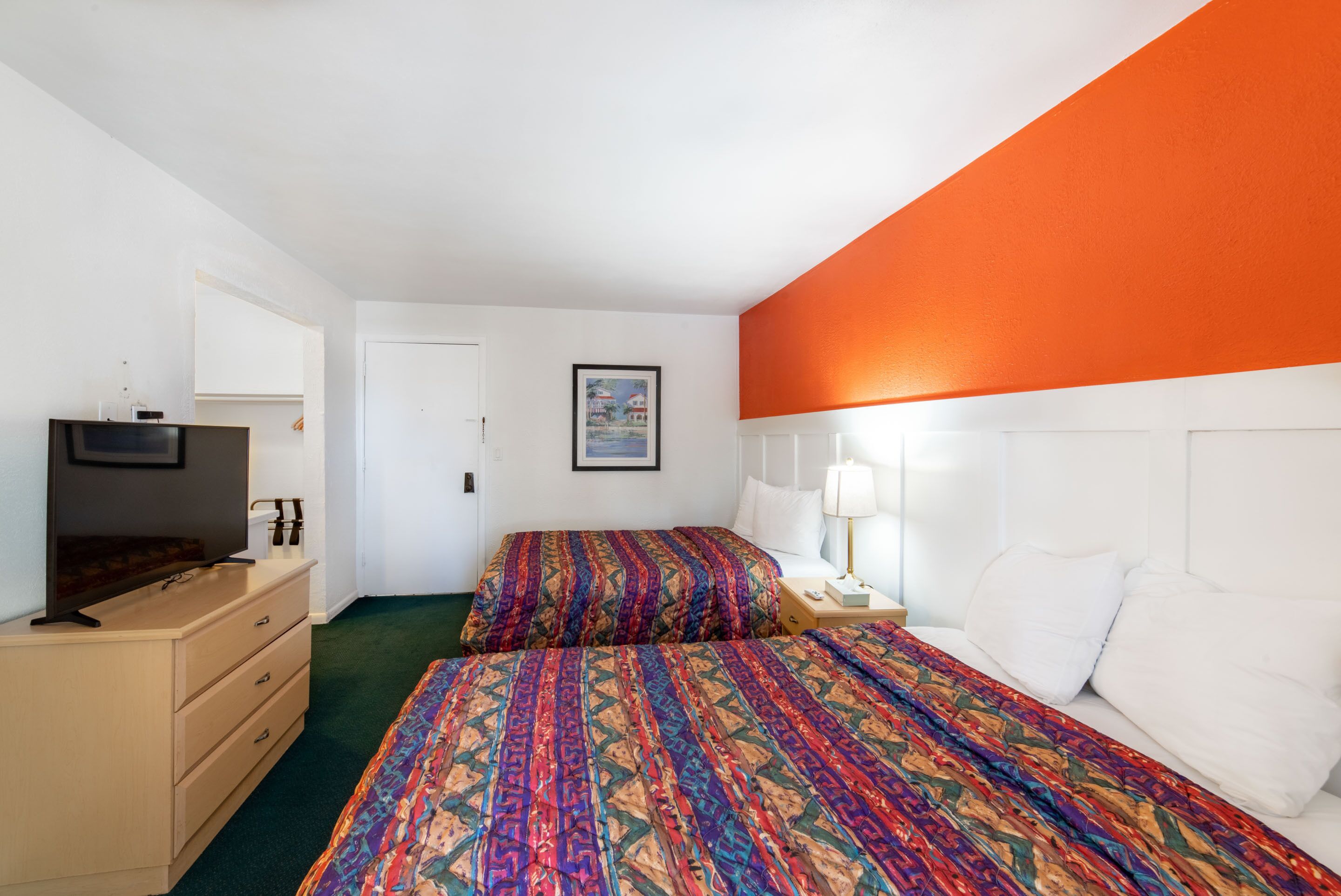 A hotel room with two beds, a TV, a dresser, and a framed picture on the wall.