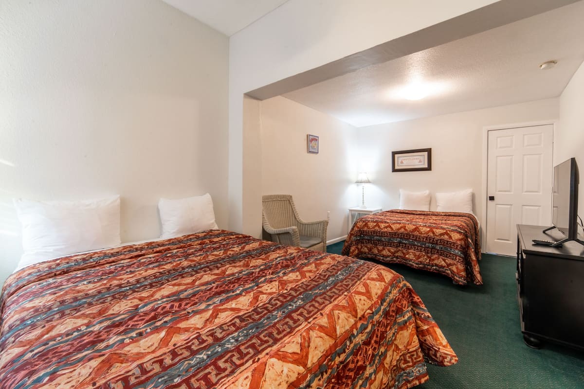 A hotel room with two beds, a chair, a desk, and a television.