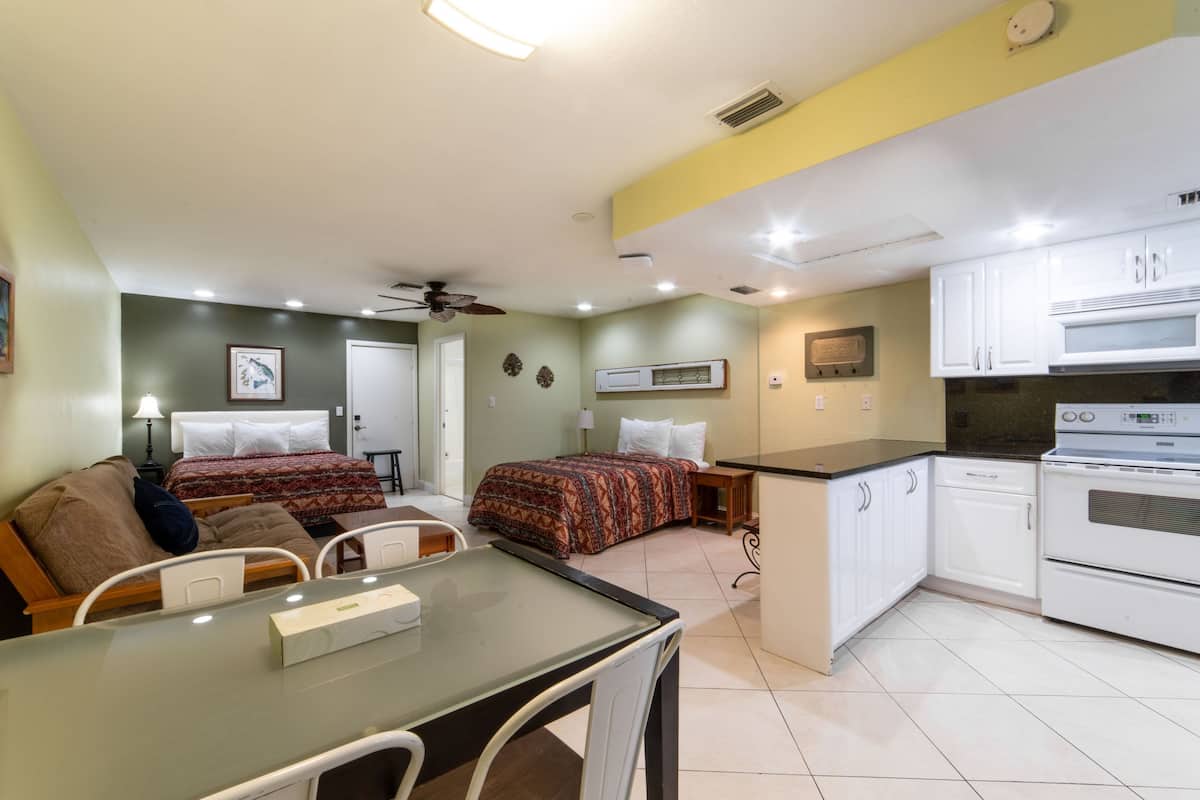 A compact hotel room with a kitchenette, a dining area, and a bed with patterned bedding.