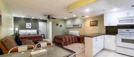A compact hotel room with a kitchenette, a dining area, and a bed with patterned bedding.
