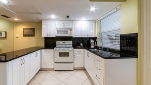 Una cocina con armarios blancos, encimera negra, estufa y microondas.