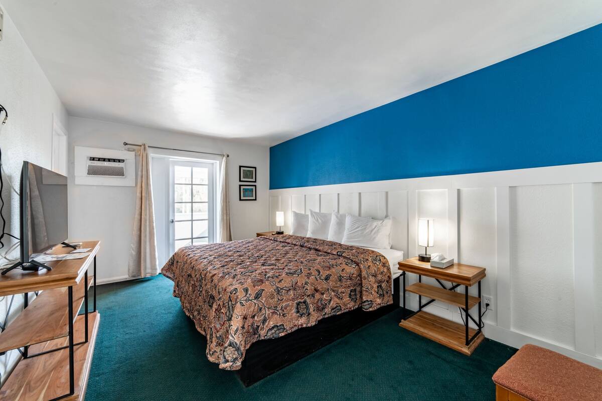 A hotel room with a bed, a desk, a chair, a TV, and a window with curtains.