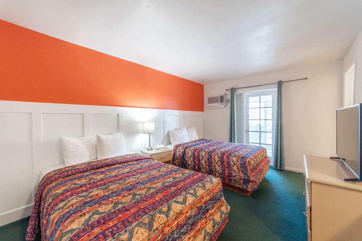 A hotel room with two beds, a TV, a desk, and a window with curtains.