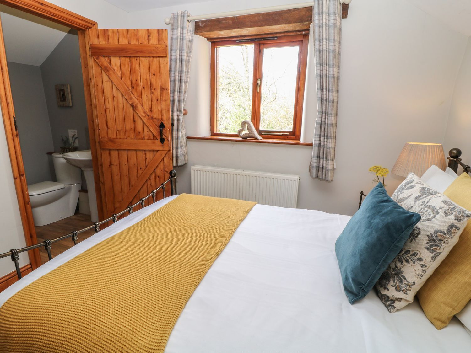 A bedroom with a bed, a window with curtains, a radiator, and a wooden door.