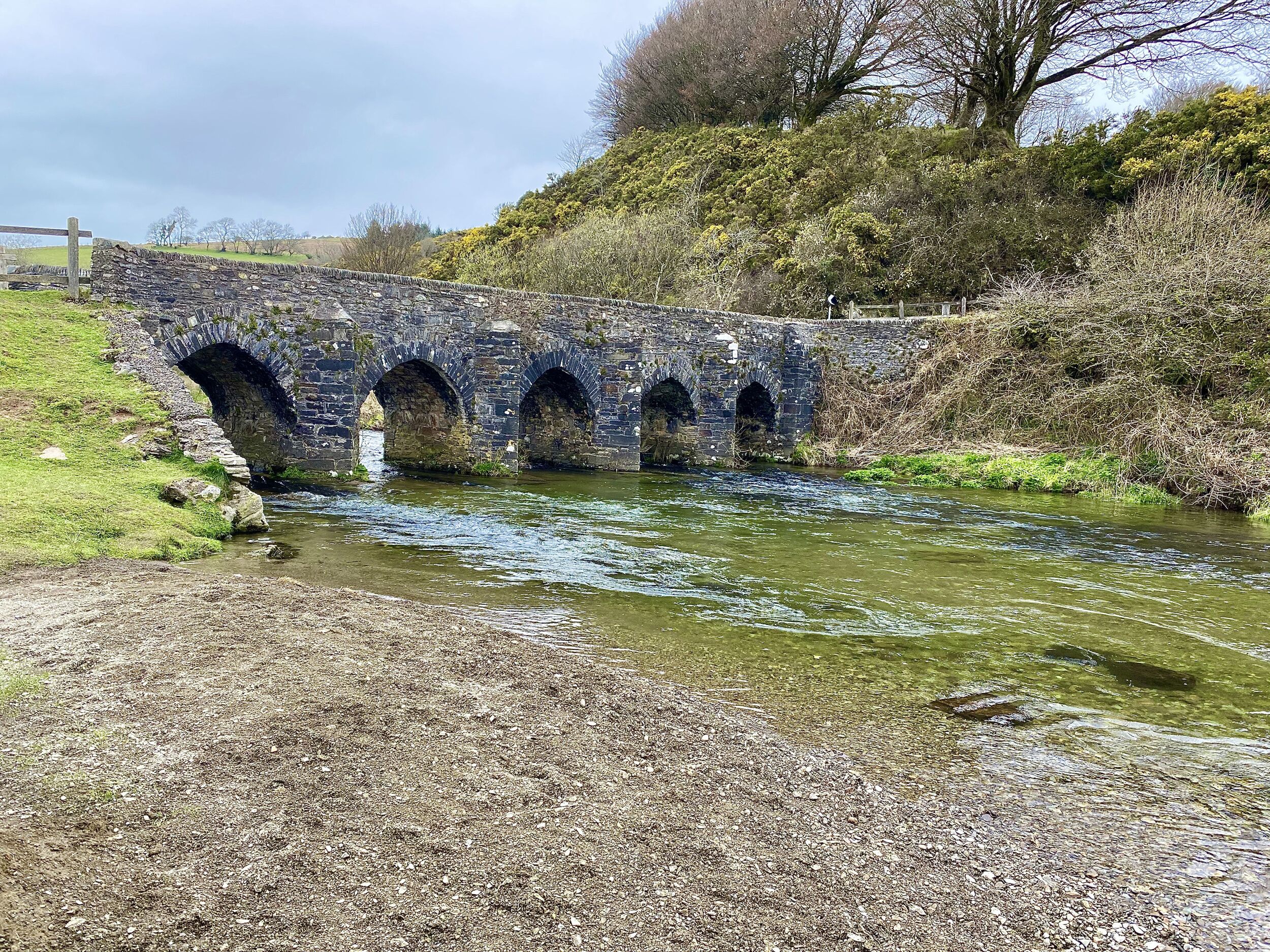 Un puente de piedra sobre un río, con un camino de grava que lo lleva.