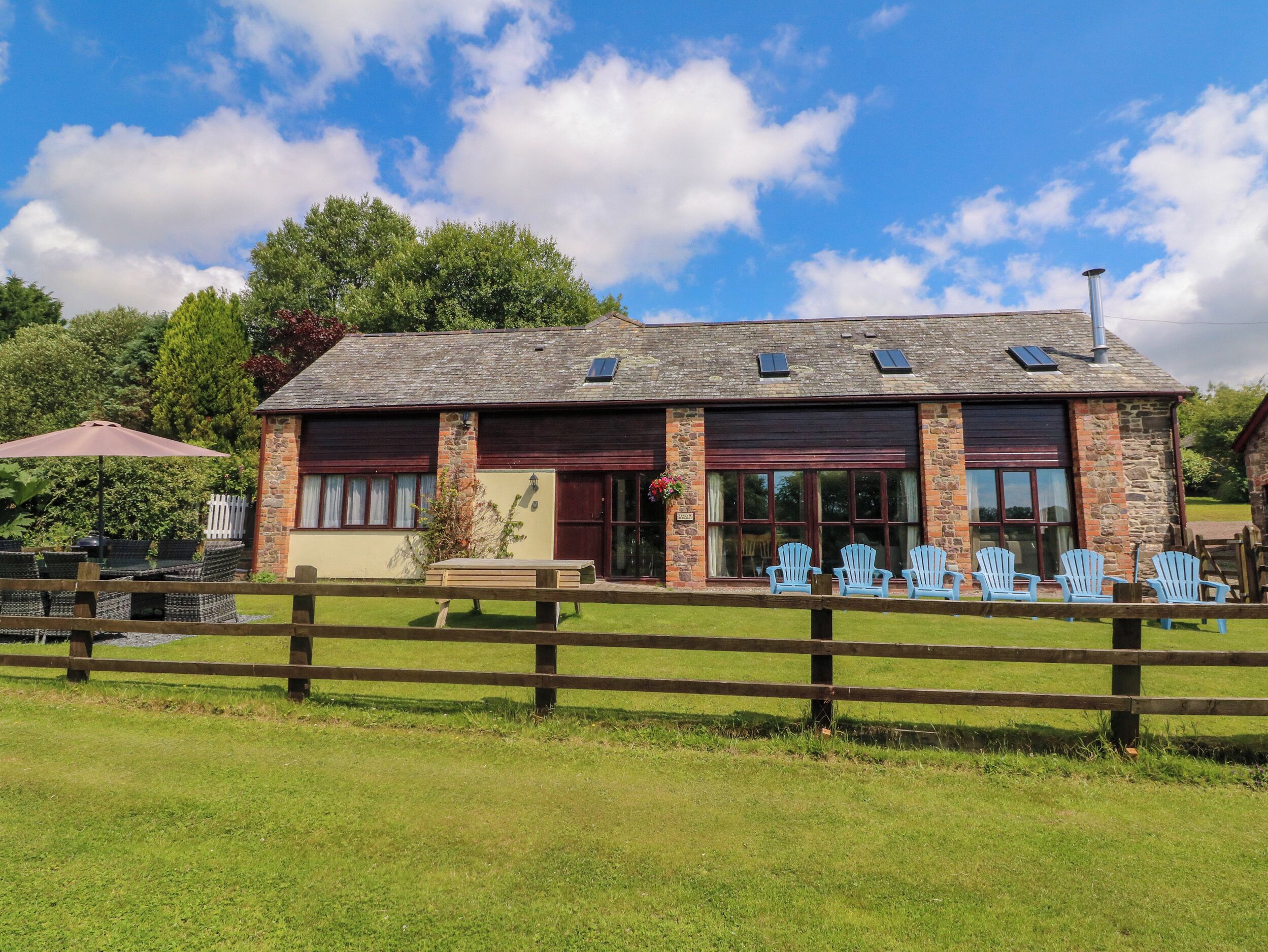 A rustic stone building with a sloped roof, large windows, and a wooden fence in the foreground.